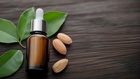 Amber glass dropper bottle with almond oil surrounded by fresh almonds and green leaves on dark wooden background for natural skincare and aromatherapy products.