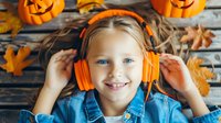 Young girl with bright orange headphones smiling at camera, wearing denim jacket against wooden background with autumn decorations, pumpkins and fall leaves.