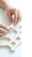 Caucasian hands assembling white wooden puzzle pieces on isolated background, representing problem solving, strategy, and business solutions for corporate design projects.