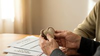 Elderly hands holding hearing aid over medical documents on wooden table in warm natural light for healthcare and aging support concepts.