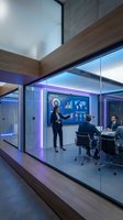 Modern glass conference room with businesswoman presenting data analytics on digital screen to corporate team in contemporary office building.