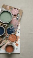 Paint cans with brushes on wooden palette showing green pink orange blue colors for home renovation and interior design projects.