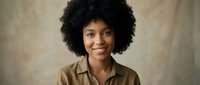 Young African American woman with natural afro hair smiling confidently, wearing casual olive shirt against neutral beige studio background.
