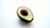 Fresh ripe avocado half with pit on white background isolated for healthy cooking and nutrition design projects.