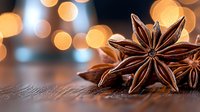 Star anise pods on rustic wooden surface with warm golden bokeh lights in background creating festive holiday atmosphere for seasonal cooking and decor.