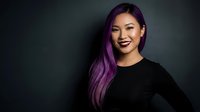Young Asian woman with vibrant purple hair smiling confidently in black top against dark background for professional headshot and portrait photography.
