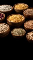 Assorted legumes and pulses in wooden bowls including chickpeas, lentils, beans and peas displayed against black background for food and nutrition content.