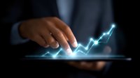 Businessman touching glowing financial chart on digital tablet screen, showing upward trend growth in blue neon light against dark background.