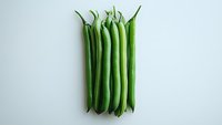 Fresh green string beans arranged in neat row on white background, isolated organic produce for healthy eating and cooking concepts.