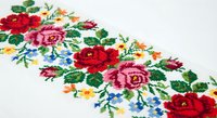 Colorful floral cross-stitch embroidery with roses and wildflowers on white fabric. Traditional needlework craft pattern for home decor and textile art projects.
