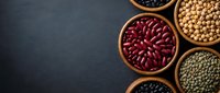 Assorted legumes and beans in wooden bowls on dark slate background for healthy cooking and nutrition concepts.