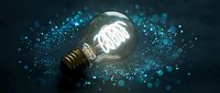 Glowing light bulb with brain filament surrounded by sparkling blue particles on dark background representing innovation and creative thinking concepts.