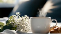 Steaming coffee cup with fresh croissant and delicate white spring flowers on windowsill in morning light, creating cozy breakfast atmosphere.