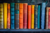 Colorful vintage hardcover books arranged on wooden shelf, featuring vibrant spines in orange, blue, yellow and pink tones against dark background. Classic literature collection.