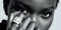 Young African American woman with dramatic eye makeup and statement ring covering part of face in black and white portrait for beauty and fashion concepts.