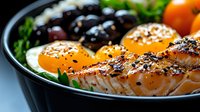 Grilled salmon fillet with sunny side up eggs, black olives and fresh herbs served in dark plate, close up view of protein-rich healthy meal.