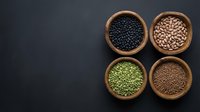 Assorted legumes and pulses in wooden bowls on dark background, including black beans, chickpeas, lentils and peas for cooking and nutrition.