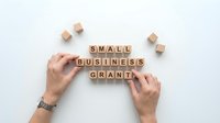 Small business grant concept with hands arranging wooden letter blocks on white background for entrepreneurship and funding applications.