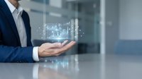 Professional businessman in suit presenting holographic financial data charts and graphs floating above open palm in modern office environment.