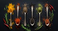 Colorful assortment of aromatic spices in silver spoons on dark background with herbs and chili peppers, top view flat lay.