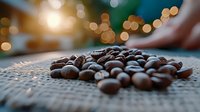 Fresh roasted coffee beans scattered on burlap textile with soft bokeh lights in background creating cozy atmosphere for cafe or coffee shop marketing.