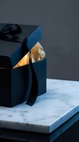Luxury dark navy gift box with black satin ribbon, glowing golden tissue paper inside, placed on marble surface for premium gifting concepts.