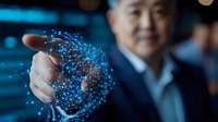 Asian businessman in suit interacting with glowing blue digital hologram sphere, demonstrating future technology and innovation in corporate environment.