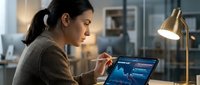 Young Asian businesswoman analyzing financial data on laptop computer in modern office during evening hours with warm desk lamp lighting.