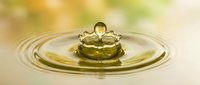 Golden water drop creating perfect ripples on calm surface with warm bokeh background capturing moment of impact and natural fluid dynamics.