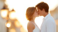 Young couple sharing intimate moment at sunset with warm golden light and romantic bokeh background for wedding or engagement concepts.