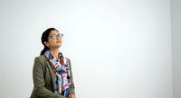 Young South Asian woman wearing glasses and olive green cardigan with patterned scarf, looking upward thoughtfully against white background. Suitable for business, education, and lifestyle projects.
