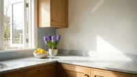 Modern kitchen corner with wooden cabinets, marble countertop, purple hyacinth flowers in white vase and fresh oranges by sunny window creating warm atmosphere.