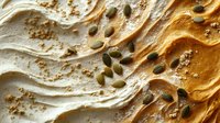 Creamy peanut butter swirl texture with scattered green pumpkin seeds creating dynamic waves and patterns, macro food photography showing rich detail and depth.