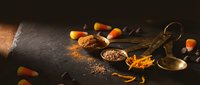 Warm spices scattered on dark wooden surface with vintage brass spoons creating cozy autumn cooking atmosphere for culinary projects and recipe designs.