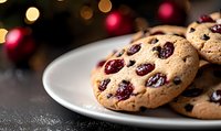 Fresh baked cranberry cookies on white plate with festive bokeh lights in background, shallow depth of field creates cozy holiday atmosphere.