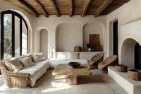 Modern Mediterranean living room with curved sofa, woven furniture, wooden beams, and arched windows creating natural light patterns on white walls.