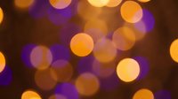 Abstract bokeh lights background with warm orange and purple glowing circles creating dreamy atmosphere for holiday decorations and festive designs.