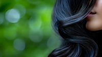 Close-up of woman with shiny dark wavy hair against soft green bokeh background for beauty and haircare concepts.