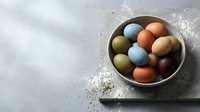 Colorful Easter eggs in rustic bowl on textured gray surface with flour dusting, perfect for spring holiday baking and cooking projects.