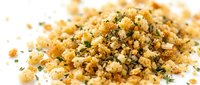 Seasoned breadcrumb mixture with herbs and spices scattered on white background, ready for coating meat, fish, or vegetables in cooking and food preparation.