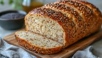 Freshly baked artisan seeded bread loaf sliced on wooden cutting board. Homemade multigrain bakery product with sesame seeds for healthy breakfast and cooking.
