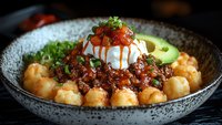 Asian fusion bowl with crispy potato gnocchi, spicy minced meat, poached egg, red sauce, microgreens and avocado served in ceramic bowl on dark background.