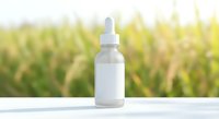 White dropper bottle with blank label on wooden surface against blurred green nature background for natural skincare and wellness product mockup.