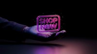 Glowing neon shop now sign held in open hand against dark background, featuring vibrant purple and pink neon lights for retail marketing and sales promotion.