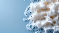 White soap foam bubbles and suds on light blue background, macro photography showing detailed texture of cleaning product lather with soft focus effect.