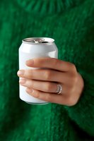 Female hand with engagement ring holding blank aluminum beverage can against green knitted sweater background, showcasing modern minimalist lifestyle.