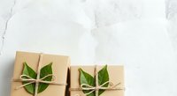 Kraft paper gift boxes tied with twine and decorated with fresh green leaves on white marble surface, suitable for eco-friendly packaging and sustainable gift wrapping designs.