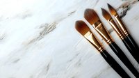 Professional makeup brushes with golden ferrules arranged on luxurious white marble surface, essential tools for beauty artists and cosmetic application.