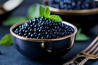 Fresh black caviar in elegant bowl garnished with mint leaf on dark slate surface. Luxury gourmet delicacy for fine dining and culinary presentations.