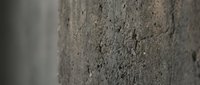 Rough textured concrete wall surface with natural imperfections and aggregate stones visible in gray cement material for construction backgrounds.